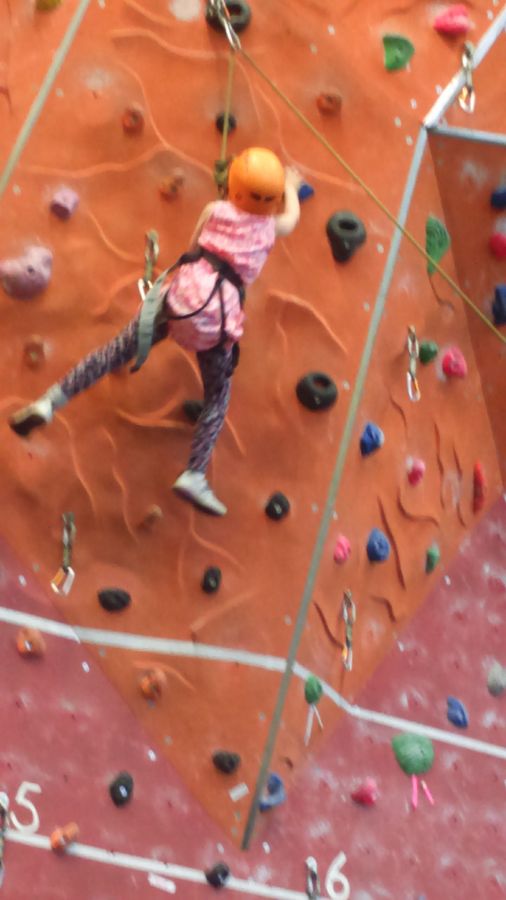 Young Ella on a climbing wall in an orange helmet