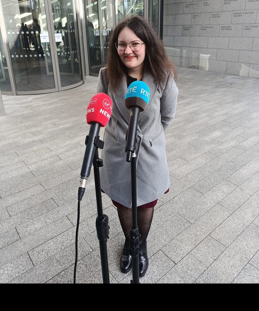 Ella smiling behind RTÉ and Virgin Media News microphones